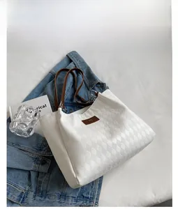 Close-up of white quilted tote bag with brown leather handles and brand emblem detail