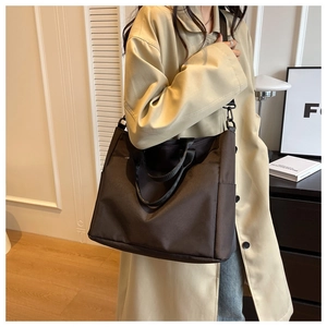Detail of a large dark brown nylon tote bag with adjustable strap in a cozy home setting