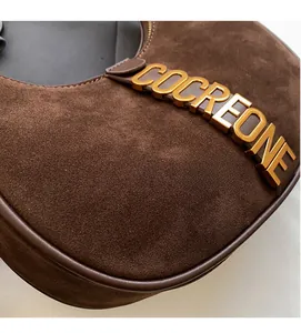 Close-up of brown suede shoulder bag with golden COCREONE logo and leather trim