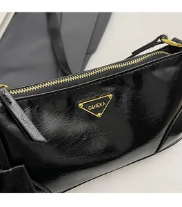 Detail of black crinkled patent leather bag with gold zip and triangle logo plate