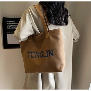 Brown canvas tote bag with deep blue lettering shown on model for size perspective