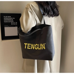 Detail of grey canvas tote bag with yellow logo on khaki trench coat model