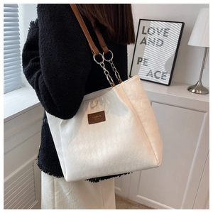 Detail of white quilted tote bag with brown leather chain strap on shoulder