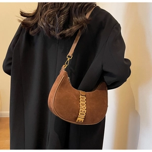 Detail of dark brown suede crescent bag with gold logo buckle on black suit jacket
