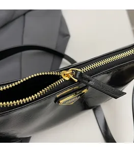 Close-up of golden zipper hardware and triangular metal logo on black patent leather bag