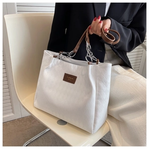 Close-up of white quilted tote bag with brown leather handles and silver chain detail