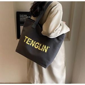 Detail of grey canvas tote bag with yellow logo print worn by model in minimalist setting