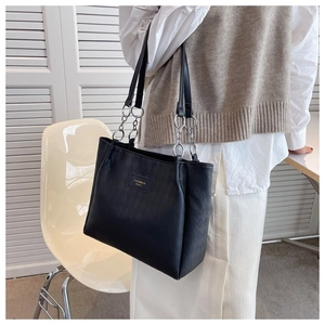 Close-up of black quilted tote bag with chain strap and metal nameplate detail