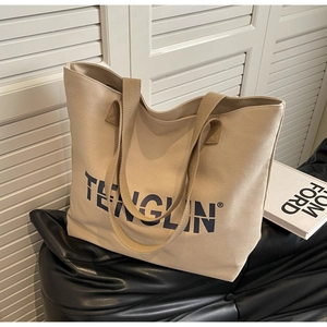 Detailed view of beige canvas tote bag with bold blue brand logo and wide web handles
