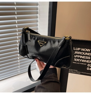 Detail of black glossy crinkled leather underarm bag with triangular metal logo plaque