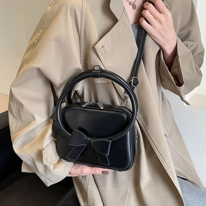 Chic black crossbody bag with large bow and round handle worn with a beige coat