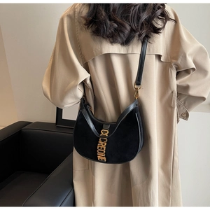 Detail of black crescent bag with gold CCCREONE logo worn over a khaki trench coat