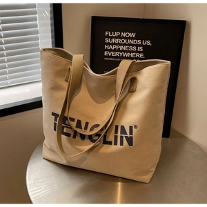 Detail of large beige canvas tote bag showing thick strap and black logo print