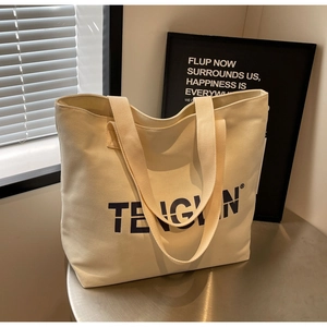 Detail of off-white canvas tote bag with black lettering logo on metallic surface