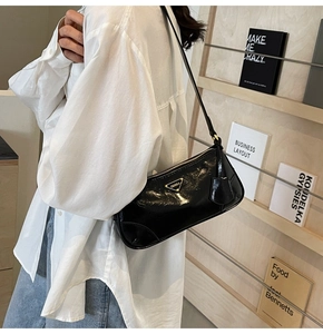 Close-up of black glossy shoulder bag with golden triangular metal plaque and leather strap