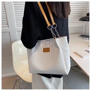 Detail of white quilted tote bag with yellow leather strap and metal chain links