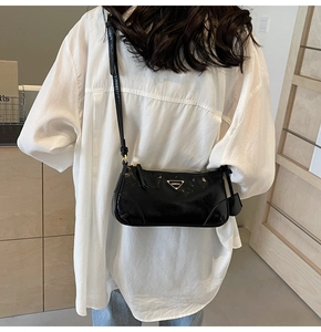 Detail of black patent leather shoulder bag with a metal triangle logo and slim strap