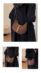 Detail of a brown suede hobo bag with a gold metal logo on a black coat background