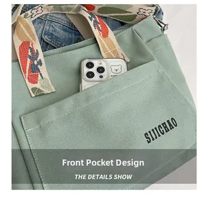 Detail of green canvas tote showing wide embroidered strap and functional front pocket