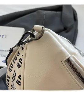 Close-up of white textured leather surface with dark gunmetal hardware and lettered strap