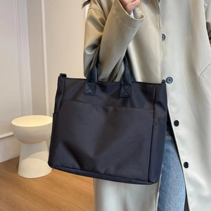 Large capacity black nylon tote bag for women shown by a model in a minimalist home setting