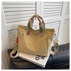 Detail of canvas tote bag with floral strap and front pocket on white books