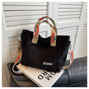 Detail of black canvas tote with jacquard strap on fashion books by white window