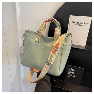Detail of light green canvas tote bag with floral embroidered wide shoulder strap