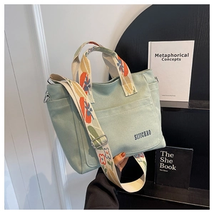 Detail of light green canvas tote bag featuring a decorative floral wide strap on a shelf