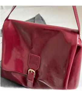 Close-up of red faux leather shoulder bag with gold metal buckle and pleated texture