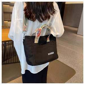 Detail of black canvas tote bag showing floral pattern strap and side pocket view