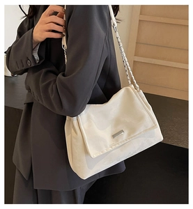 Detail of white leather shoulder bag featuring silver chain strap and metal plaque