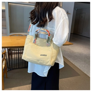 Detailed side view of beige canvas tote bag with artistic colorful pattern strap on model