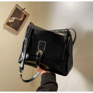 Close-up of black glossy leather crossbody bag with decorative metal buckle and strap