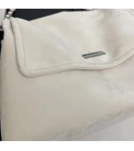 Close-up of beige suede shoulder bag featuring detailed stitching and metal logo plate