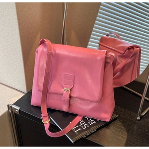 Pink matte leather crossbody bag with fold-over flap and buckle detail on dark wood surface