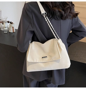 Detail of white leather shoulder bag with woven chain strap and silver metal logo plate