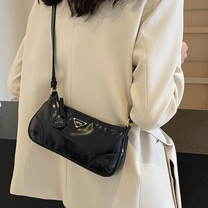 Glossy black underarm bag with triangle metal logo worn on cream blazer for high-end look