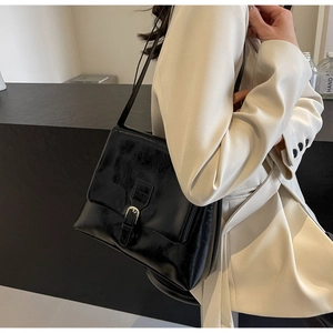 Close-up of a glossy black crossbody tote bag featuring a metallic silver buckle detail