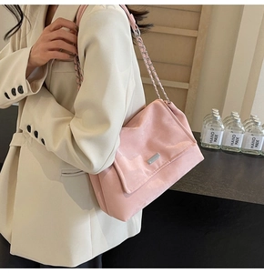 Detail of pink suede tote bag with silver chain strap worn by a model in a beige suit