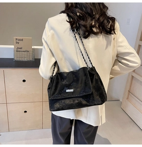 Detail of black textured tote bag featuring silver chain strap and metal clasp on model