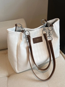 White quilted tote bag with brown leather straps and metal chain on a beige sofa