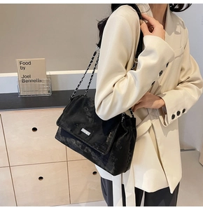 Detail of black velvet crossbody tote with chain strap shown on a shoulder