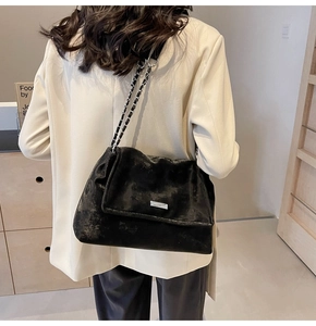 Detail of black suede tote bag featuring silver chain strap and metal logo plaque