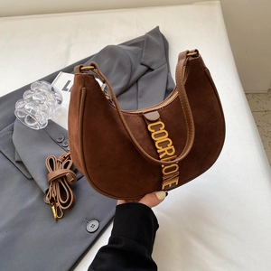 Brown suede crescent bag with gold metal logo on a grey blazer, 45-degree angle view