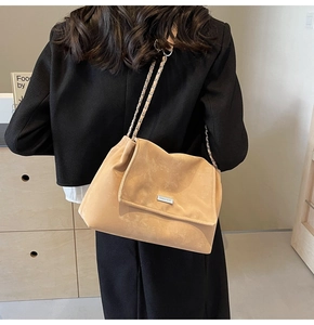 Detail of suede crossbody tote with metal chain strap and logo plate for daily wear