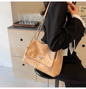 Close-up of a beige tote bag with distressed texture and metal chain strap on a model