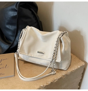 Close-up of cream tote bag with silver chain strap and metal logo on stone surface