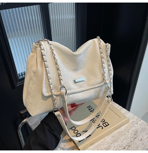 Detailed close-up of ivory tote bag featuring silver chain strap and metal logo plaque
