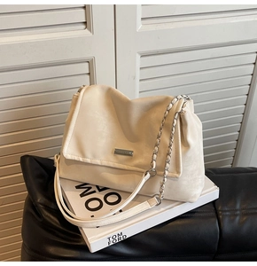 Close-up of cream-white leather tote bag featuring a metal logo and chain strap detail